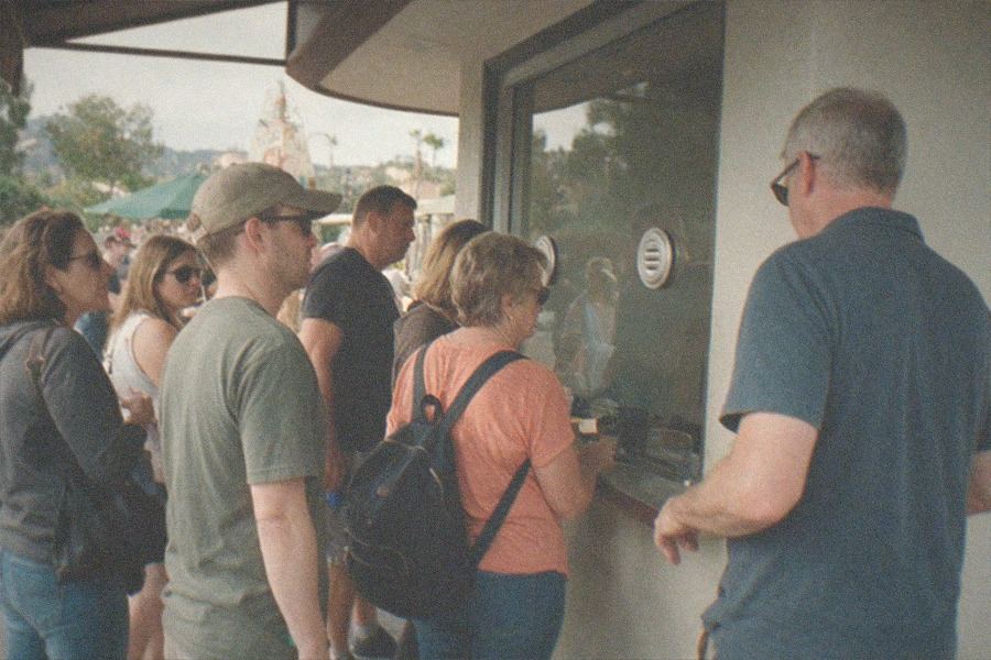 Visitors walk along an outdoor boardwalk beside harbor water with the aquarium building behind