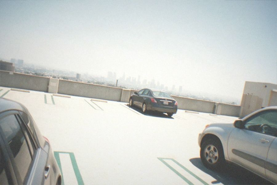 A studio entry gate with a guard booth and parked cars in morning light