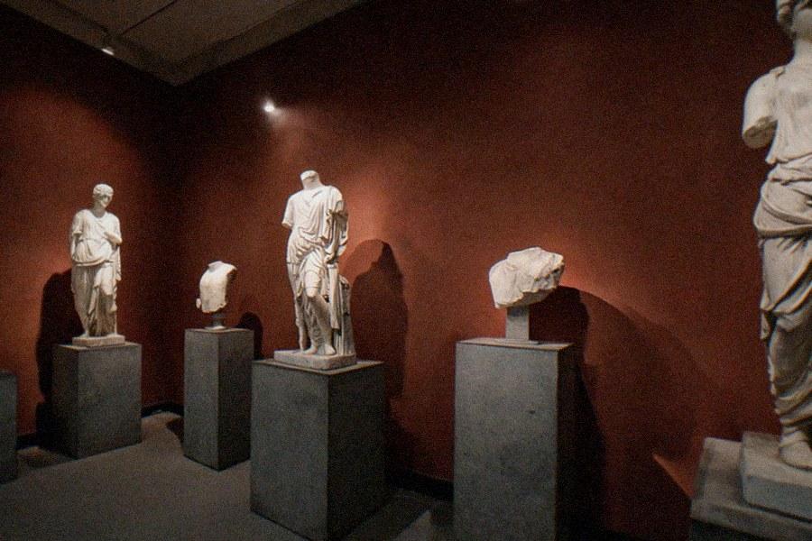 A gallery in The Getty Villa with ancient marble statues and Roman fresco walls under a coffered ceiling
