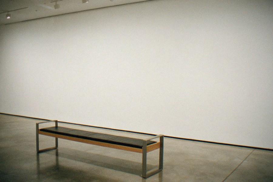 Sunlit museum gallery with sculptures on pedestals and visitors viewing large canvases.