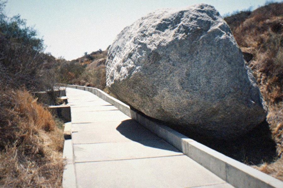 Visitors walking beneath the massive suspended boulder of the Levitated Mass installation at LACMA